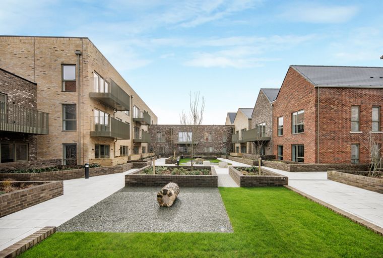 A courtyard with modern brick buildings, paved walkways, and green lawns.