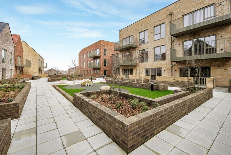 A courtyard with modern brick apartment buildings and landscaped garden beds.