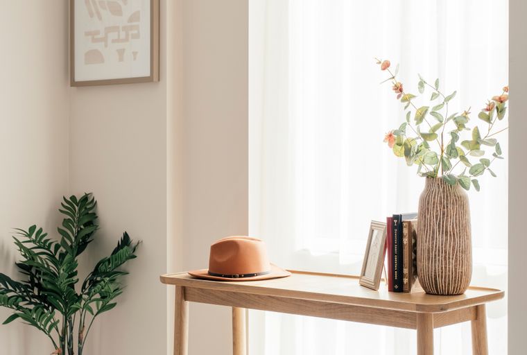 A corner of a room with a console table, a plant, and a window with sheer curtains.