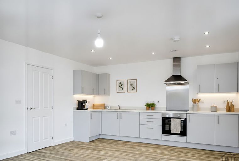 A modern kitchen with light grey cabinets, a stainless steel oven, and wooden flooring.