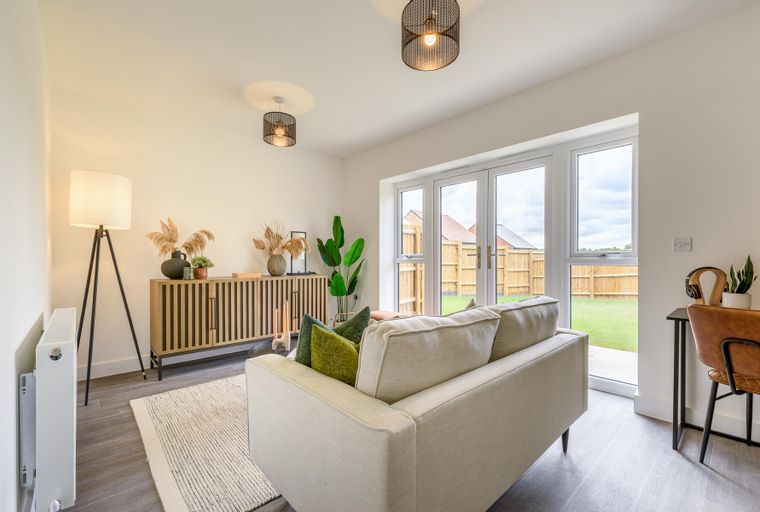 A living room with a sofa, sideboard, floor lamp, and French doors leading to a backyard.