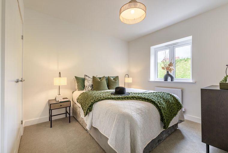 A bedroom with a bed, pillows, a green throw, bedside tables, lamps, a window, and a dresser.