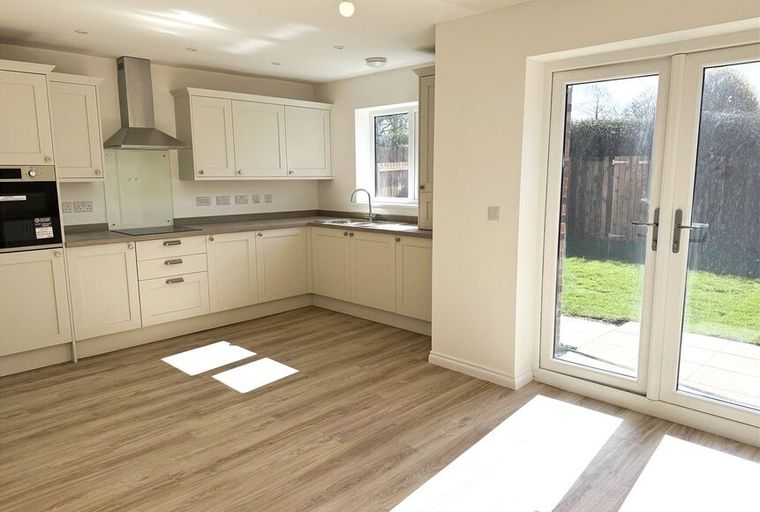A kitchen with cream cabinets, a stainless steel range hood, and French doors leading to a garden.