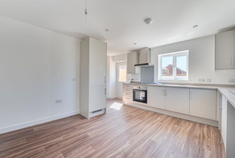 A modern kitchen and dining area with light-colored cabinets, a window, and wood-effect flooring.