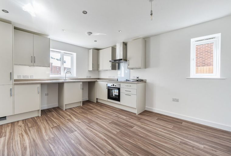 A modern kitchen with cream cabinets, countertops, an oven, and wood-effect flooring.