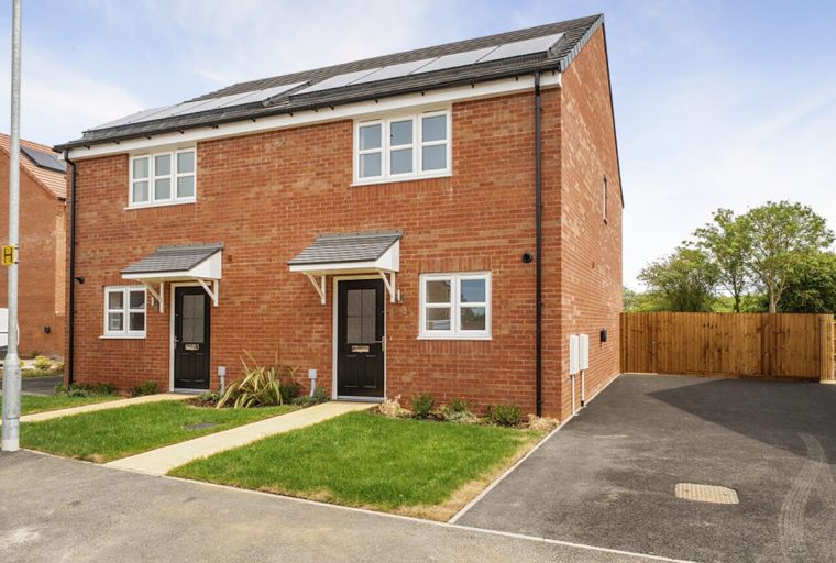 A red brick semi-detached house with solar panels on the roof and a black front door.