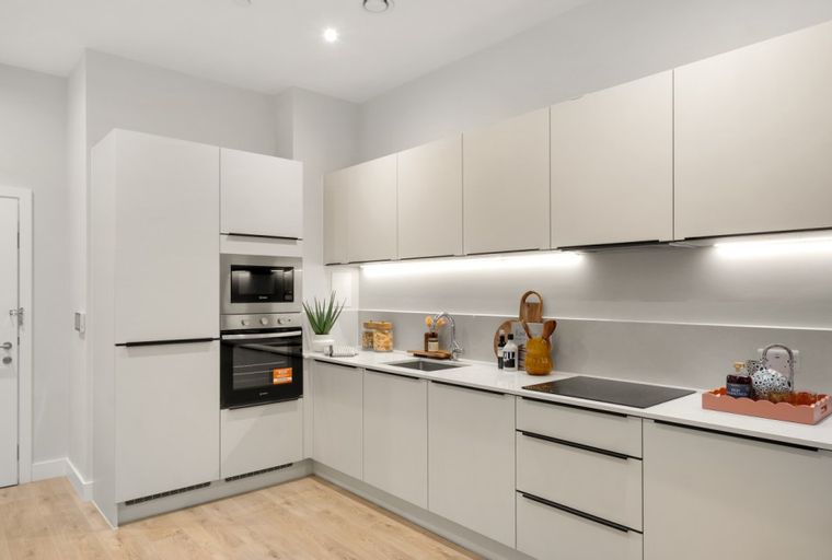 A modern kitchen with white cabinets, an oven, and a sink.