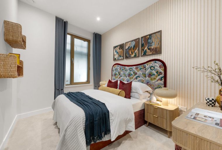 A bedroom with a bed, pillows, a throw blanket, and a bedside lamp.