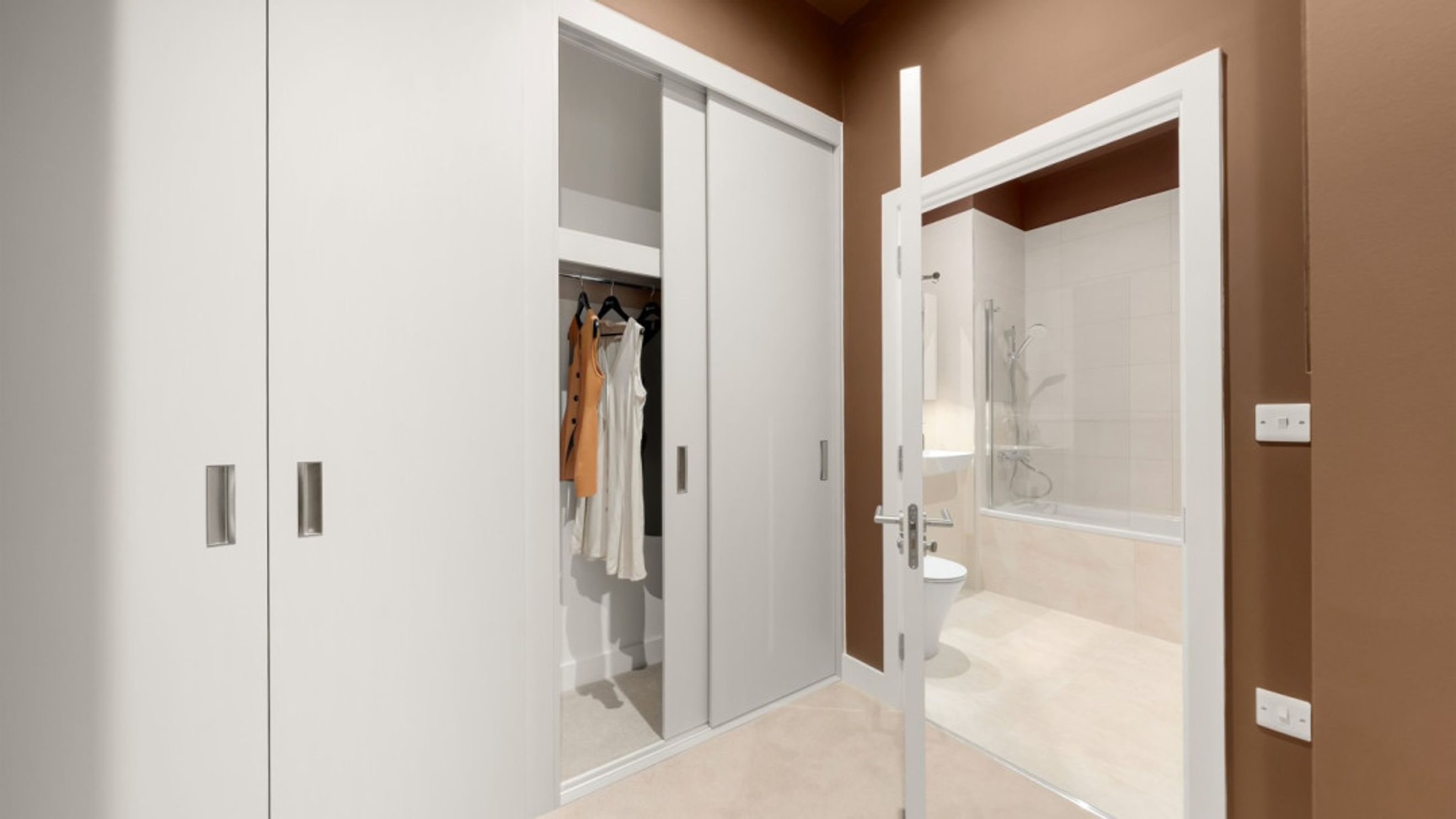 A hallway with a closet and an open bathroom door revealing a toilet and bathtub.