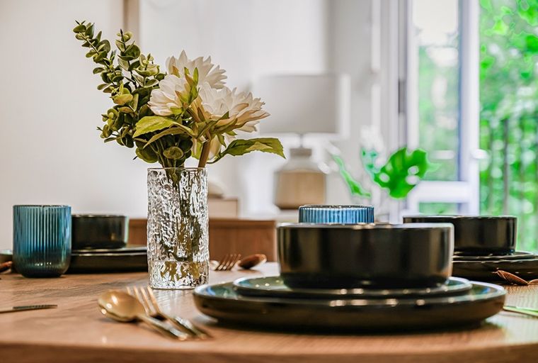 A dining table set with black plates, bowls, gold cutlery, and a vase of flowers.