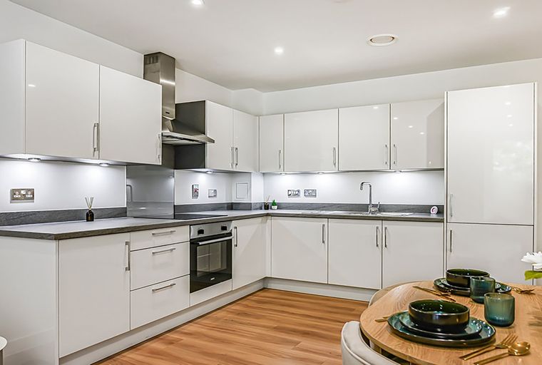 A modern white kitchen with dark countertops and a dining table set for a meal.