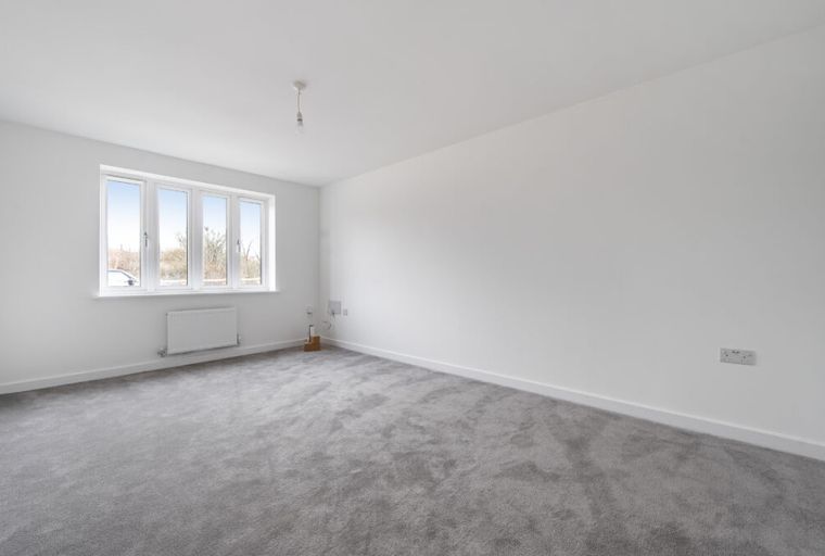 A spacious, unfurnished room with grey carpet and a large window.
