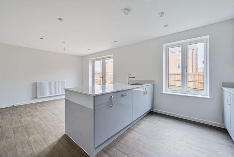 A modern kitchen and living area with a grey island, white radiator, and wood-effect flooring.