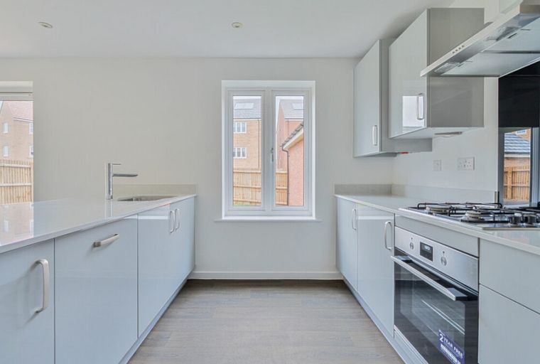 A modern kitchen with grey cabinets, white countertops, a gas hob, and a window.