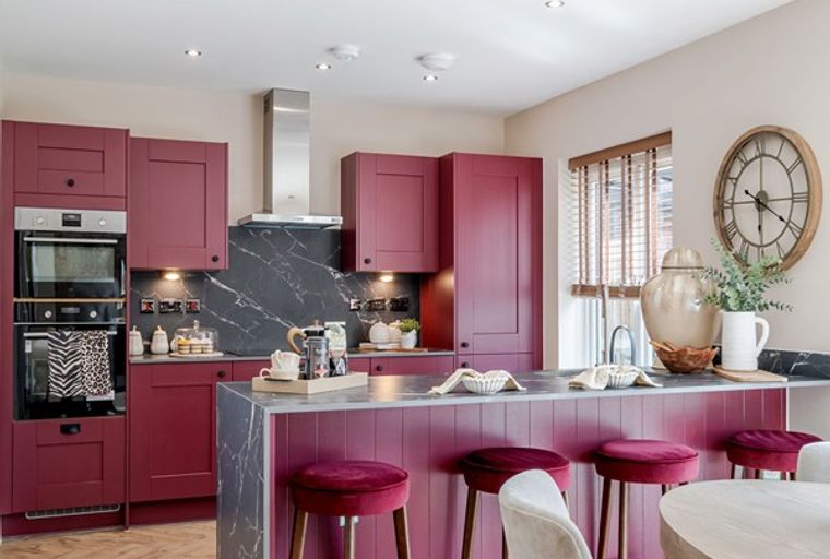 A modern kitchen with deep red cabinets, a marble backsplash, and an island with bar stools.