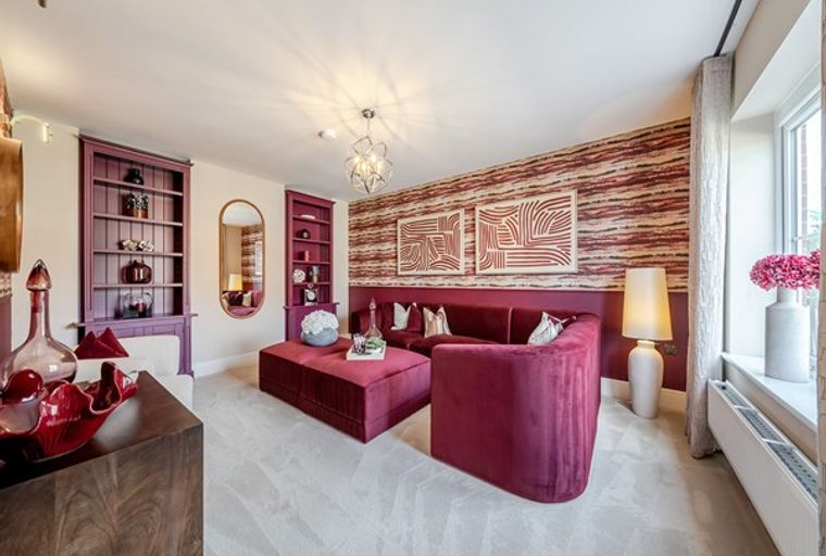 A living room with a burgundy sectional sofa, ottoman, built-in shelves, and abstract art.