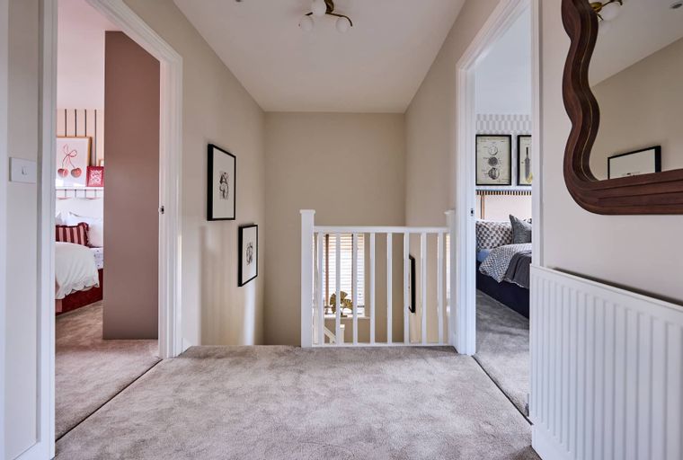 A hallway with two open doorways leading to bedrooms, a white railing, and framed artwork on the walls.