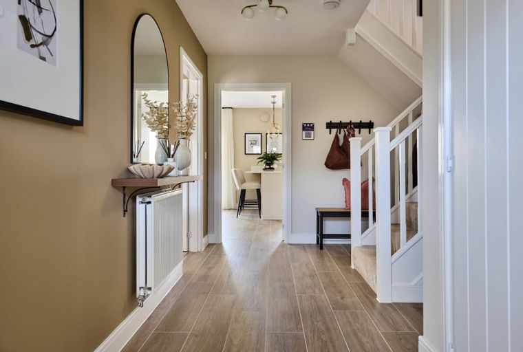 A hallway with a mirror, radiator, coat rack, and stairs leading to the upper floor.
