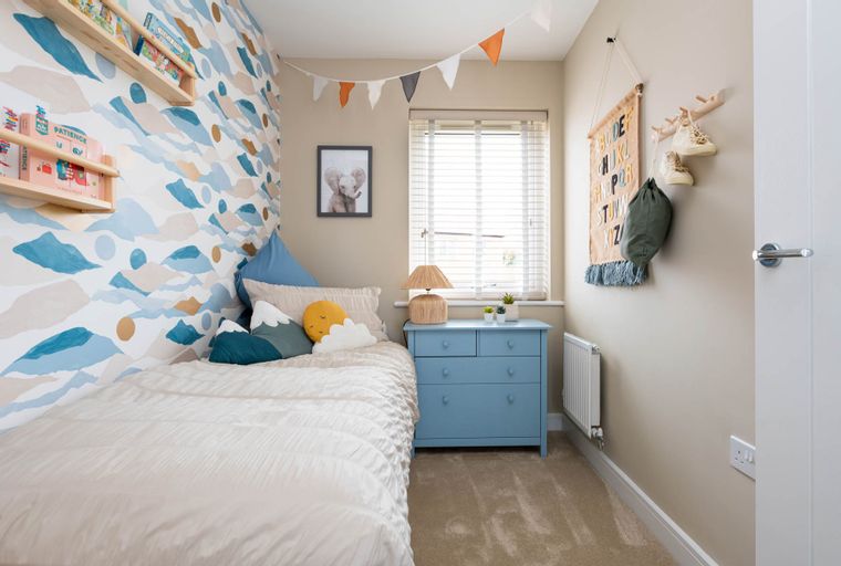 A child's bedroom with a bed, dresser, and decorative wallpaper.