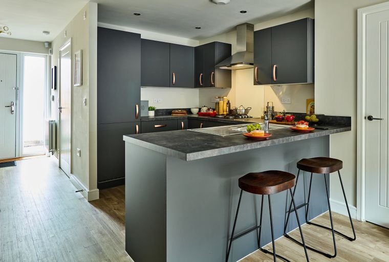 A modern kitchen with dark grey cabinets, a stone-effect countertop, and a breakfast bar with stools.