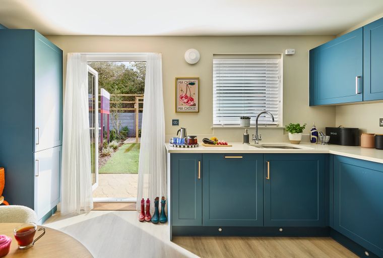 A modern kitchen with teal cabinets, a sink, and a doorway leading to a garden.