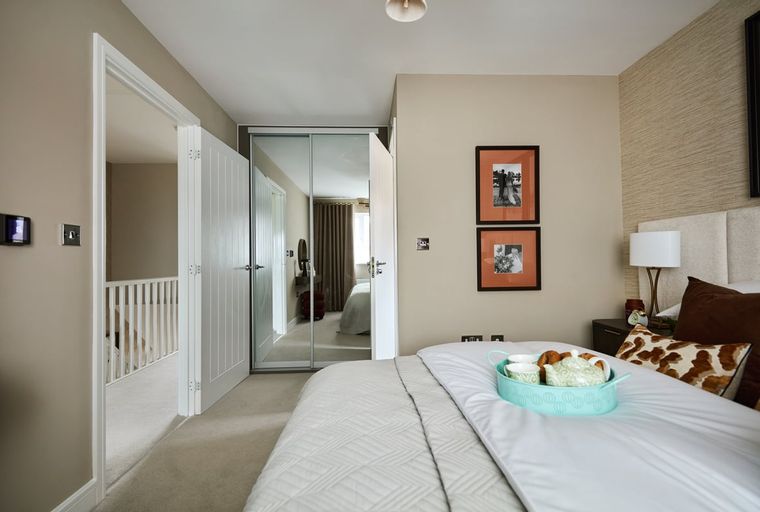 A bedroom with a bed, mirrored wardrobe, and framed pictures on the wall.