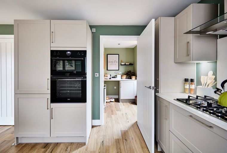 A modern kitchen with light gray cabinets, integrated ovens, and a gas hob.