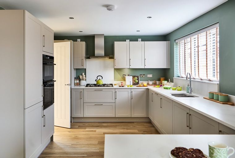 A modern kitchen with light-colored cabinets, integrated ovens, and a stainless steel range hood.
