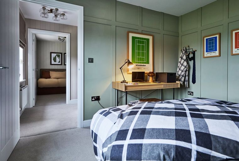 A bedroom with a desk, a laptop, a poster, and a bed with a plaid duvet.