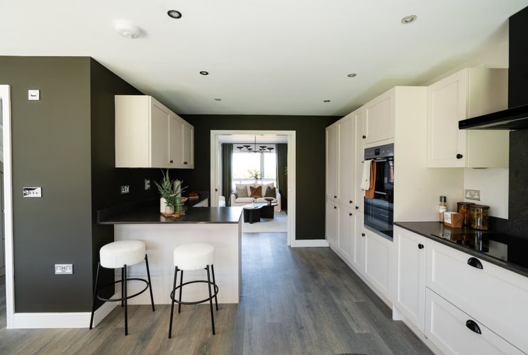 A modern kitchen with cream cabinets, a breakfast bar, and integrated appliances, opening into a living room.