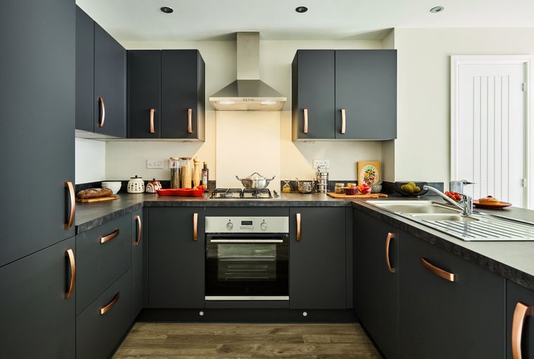 A modern kitchen with dark grey cabinets, copper handles, a gas hob, and a double sink.