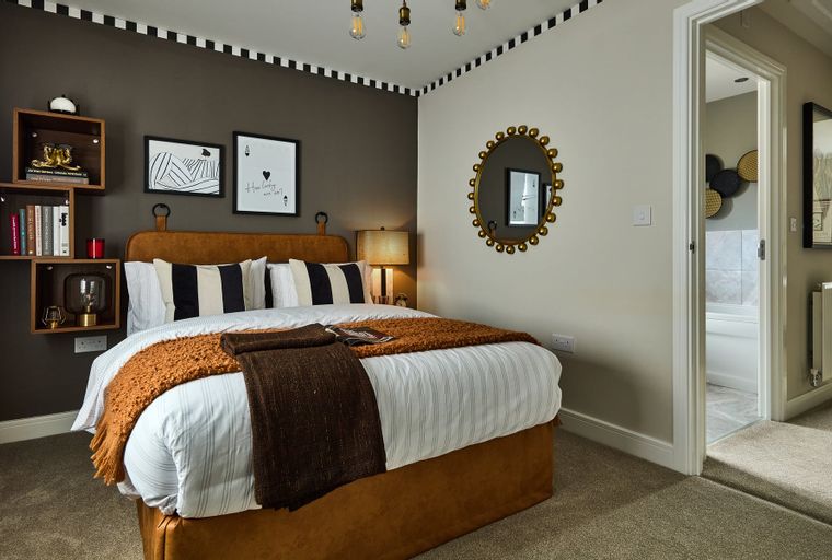 A bedroom with a bed, pillows, throws, wall art, and a mirror.