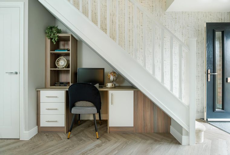 A home office setup under a staircase with a desk, chair, and shelving.