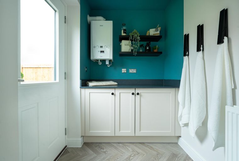 A laundry room with a gas boiler, cabinets, shelves, and towels hanging on the wall.