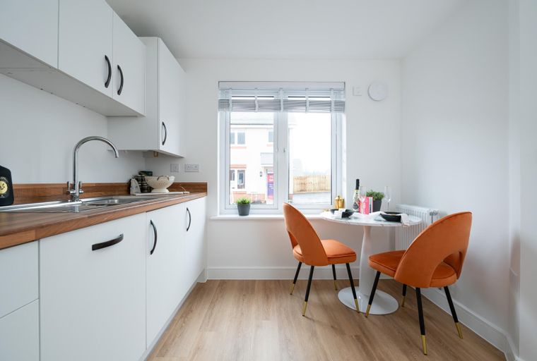 A kitchen and dining area with white cabinets, a wooden countertop, a sink, a marble-top table, and two orange chairs.
