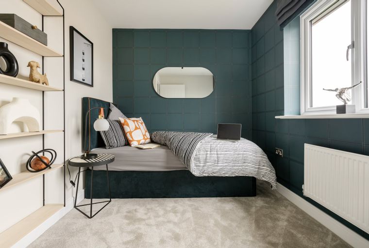 A bedroom with a bed, pillows, a laptop, and a side table.