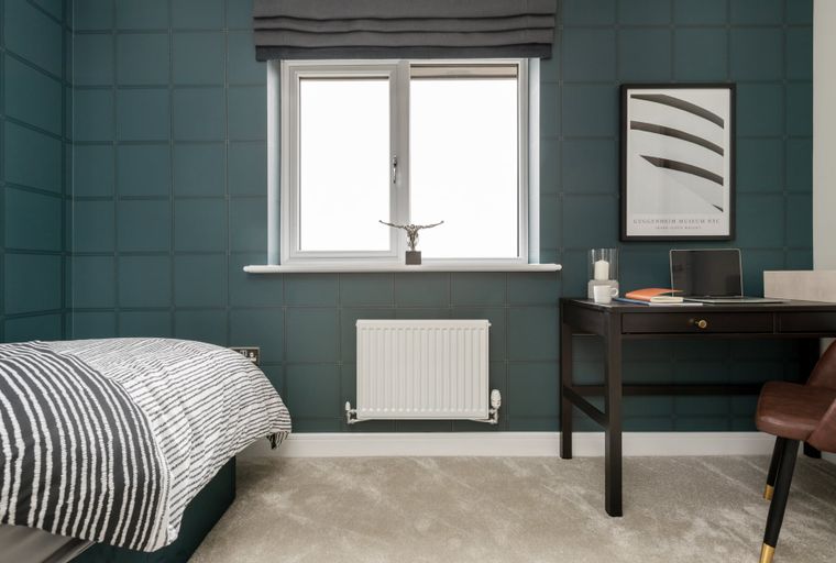 A bedroom with a bed, a desk, a window, and a radiator.