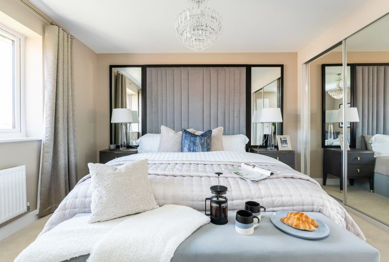 A bedroom with a bed, bedside tables, lamps, and mirrored wardrobes.