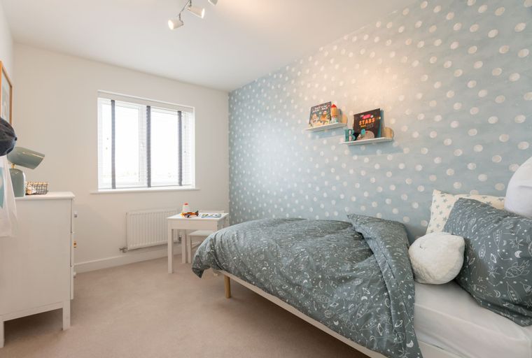 A child's bedroom with a bed, desk, and polka dot wallpaper.
