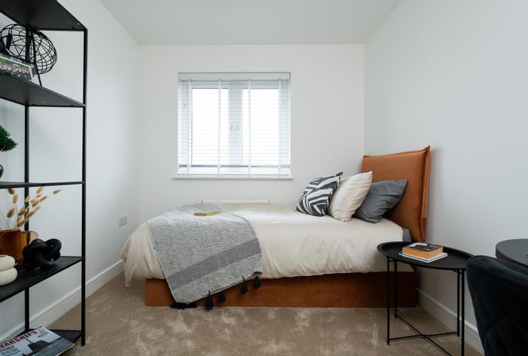 A bedroom with a bed, pillows, a throw blanket, a window, and a shelving unit.