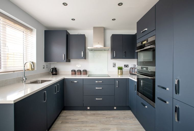 A modern U-shaped kitchen with dark blue cabinets, a quartz countertop, and integrated appliances.