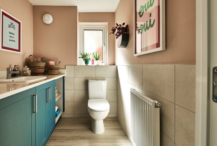A bathroom with a teal vanity, sink, toilet, and window.