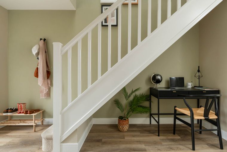 A home entryway with a shoe rack, coat rack, and a desk under the stairs.