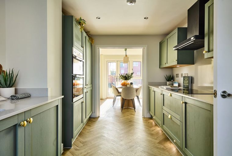 A modern kitchen with sage green cabinets, integrated ovens, and a herringbone floor.