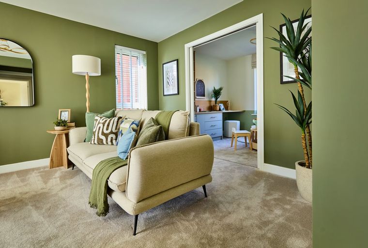 A living room with a sofa, floor lamp, and mirror, adjacent to a home office with a desk and chair.