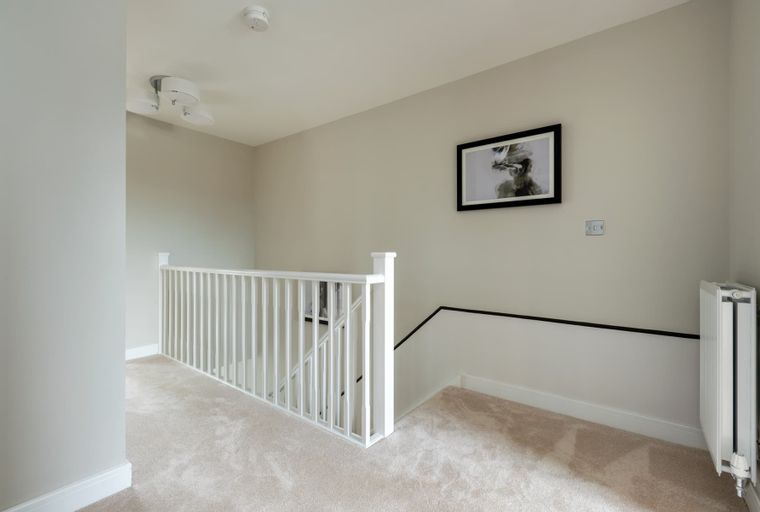A hallway with a carpeted floor, a white banister, and a framed picture on the wall.