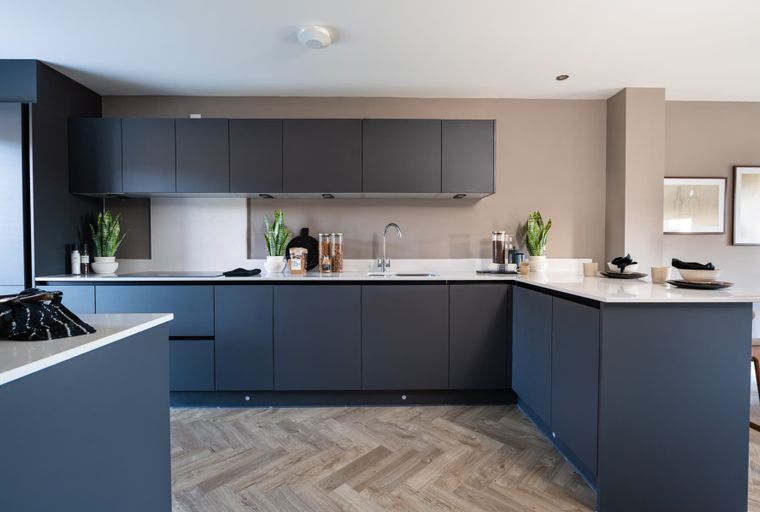 A modern kitchen with dark grey cabinets, white countertops, and a herringbone wood floor.