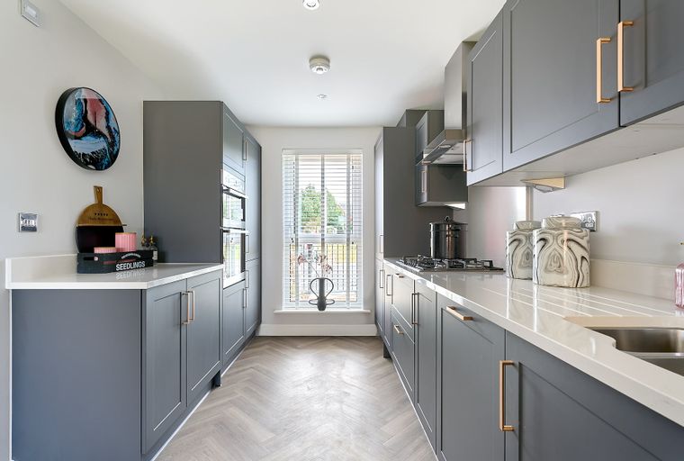 A modern grey kitchen with white countertops, integrated ovens, and a herringbone floor.