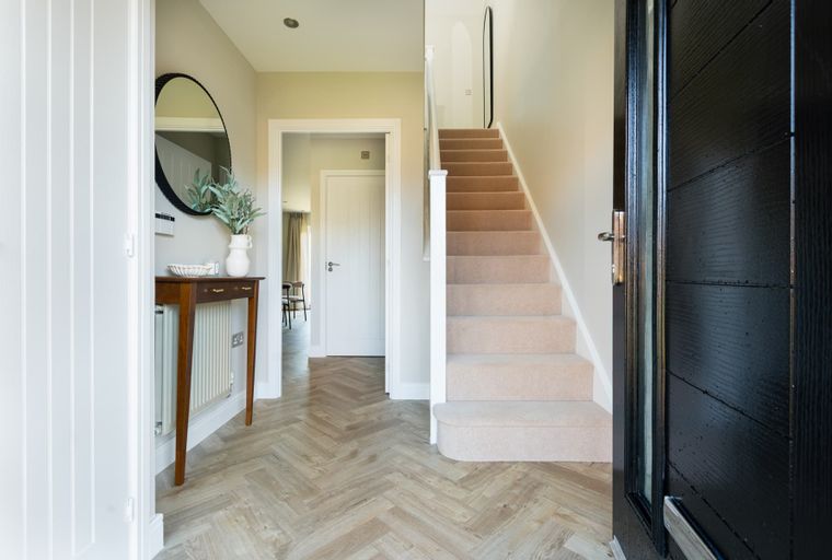 A hallway with a console table, mirror, staircase, and a black front door.