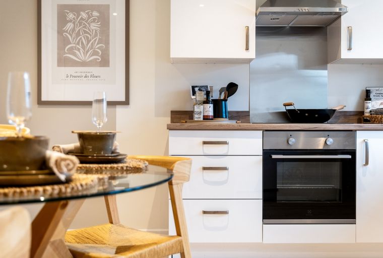 A modern kitchen with white cabinets, a built-in oven, and a dining area.